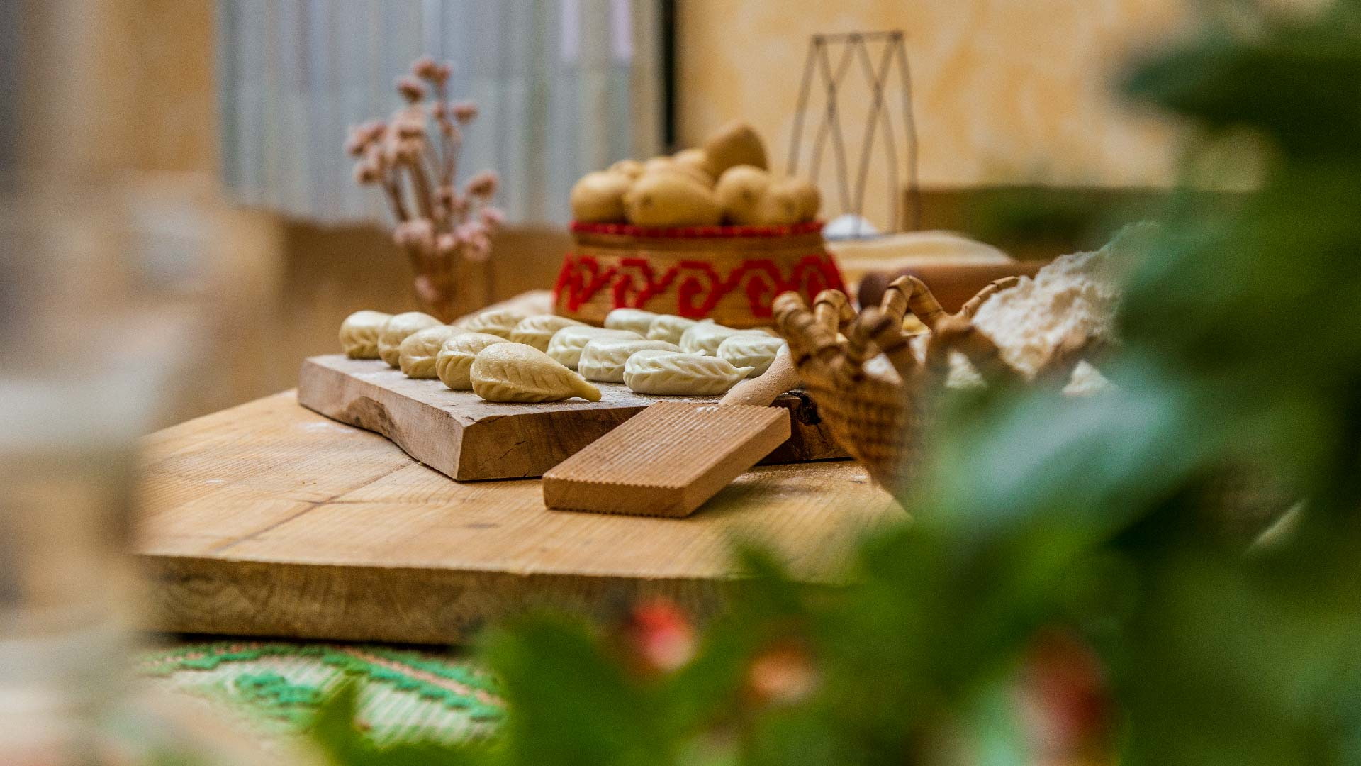 Culurgiones appena chiusi a mano su un tagliere di legno, accanto a farina e cestino tradizionale